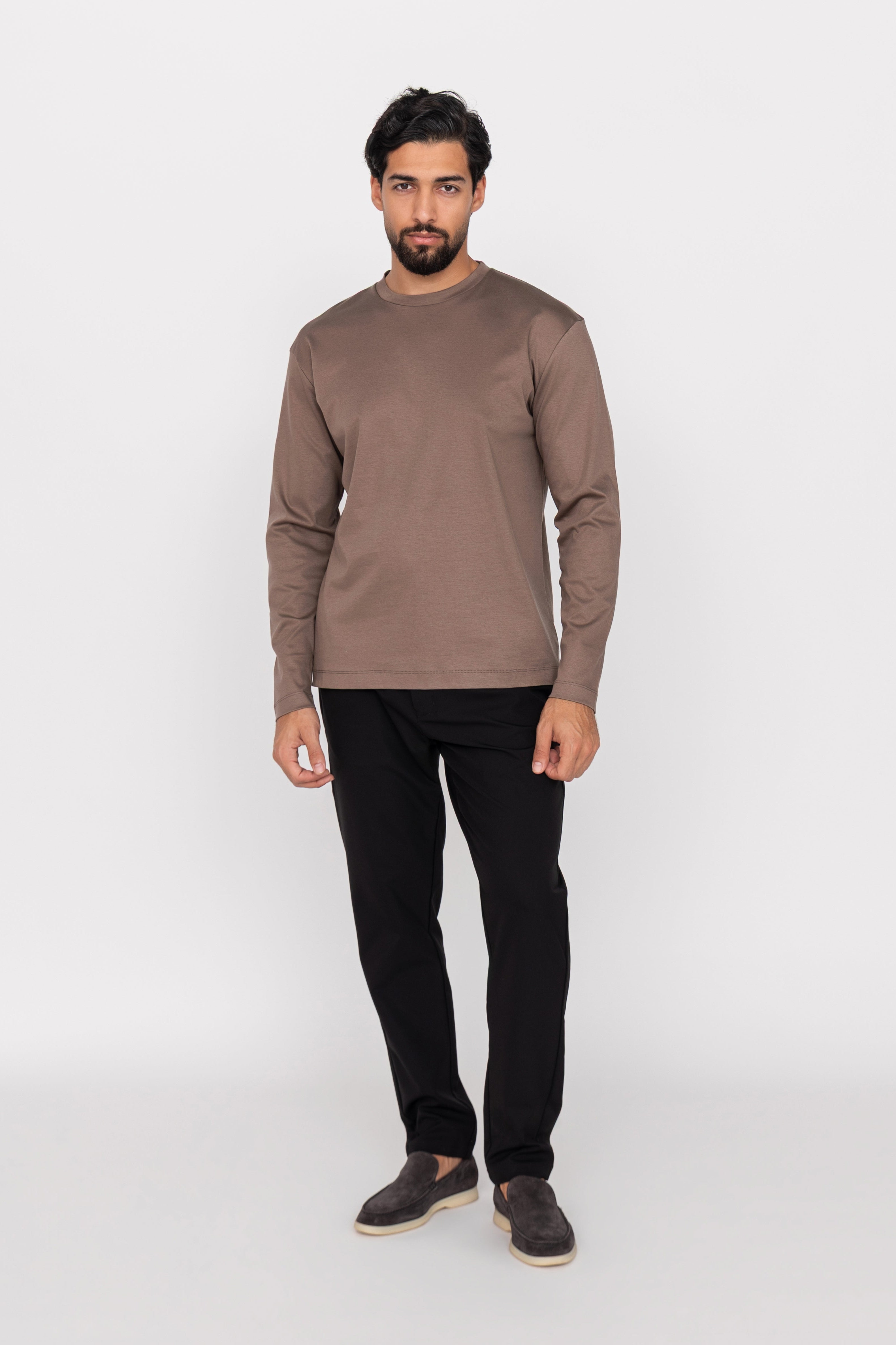 Man wearing a brown long-sleeve shirt and black pants on a white background