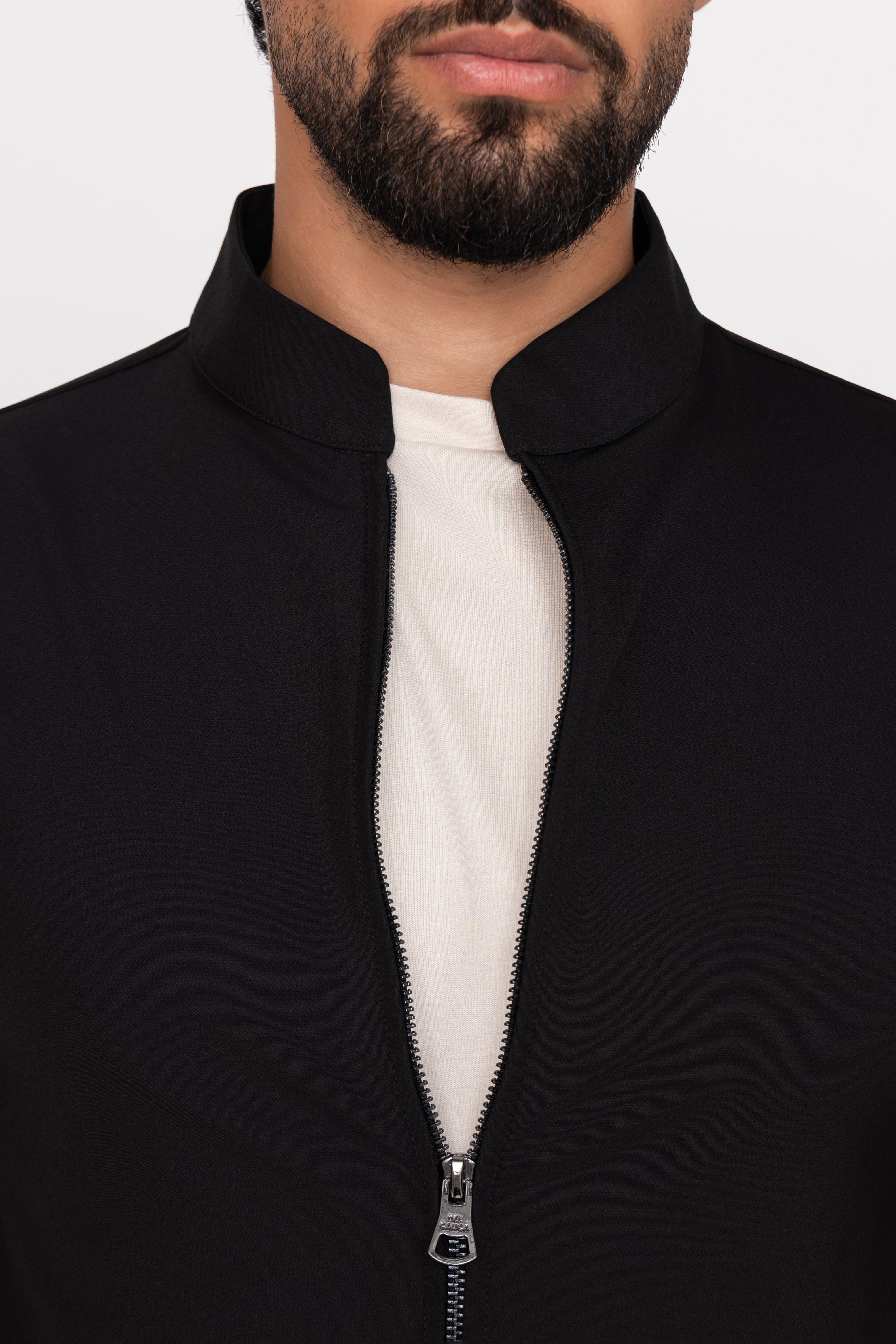 Person wearing a black jacket with a white shirt underneath on a plain background