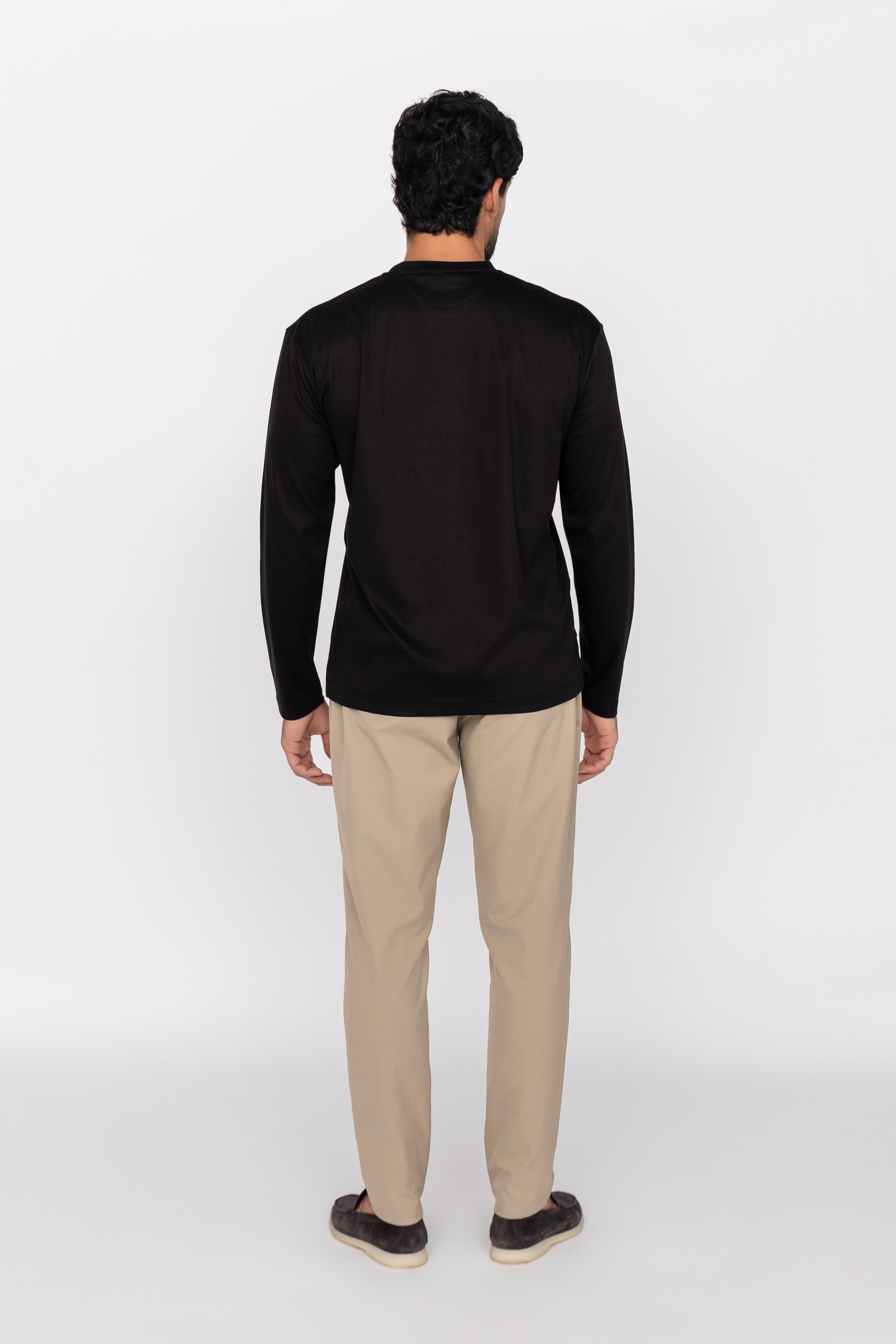 Man wearing a black long-sleeve shirt and beige pants on a white background