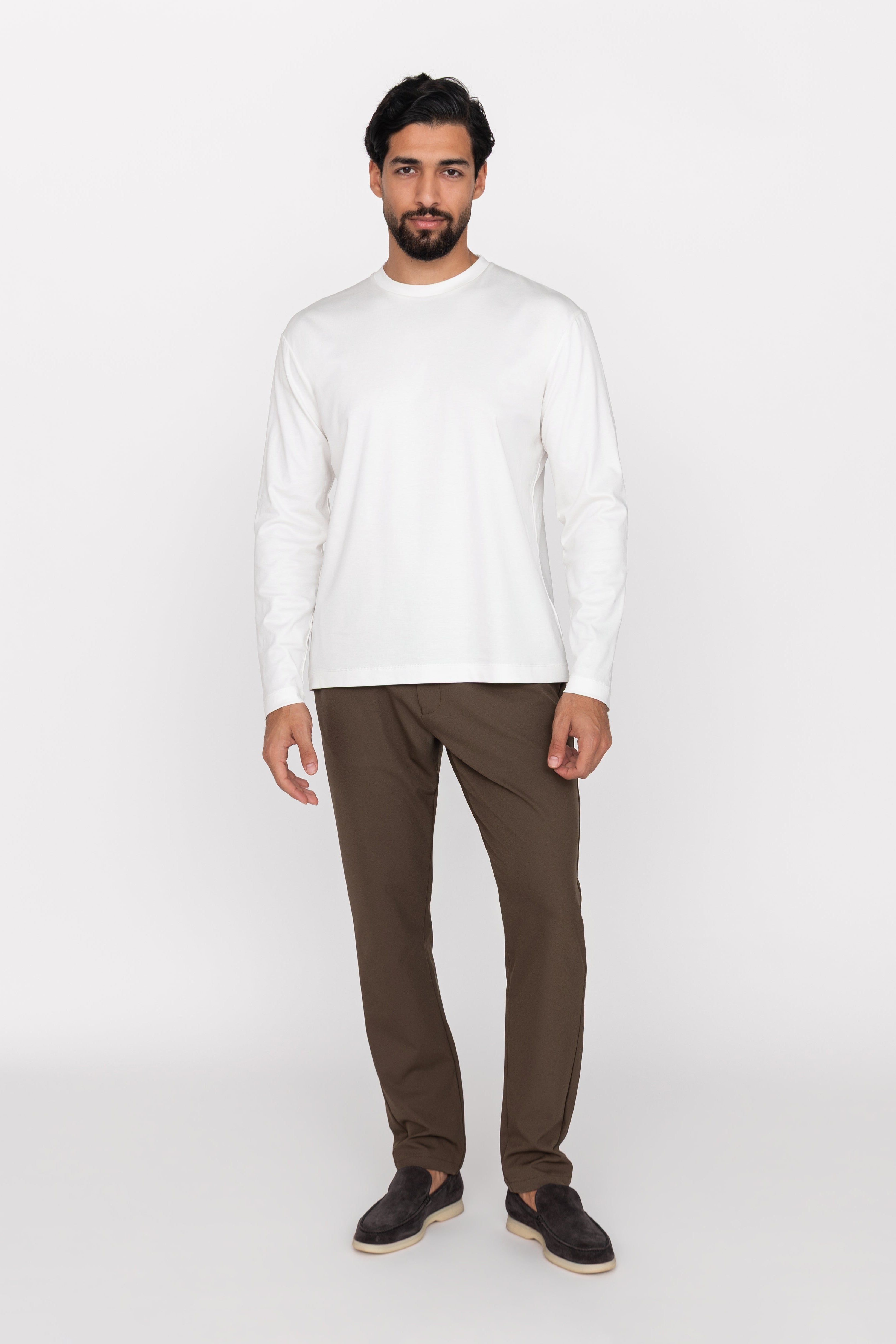 Man wearing a white long-sleeve shirt and brown pants on a white background