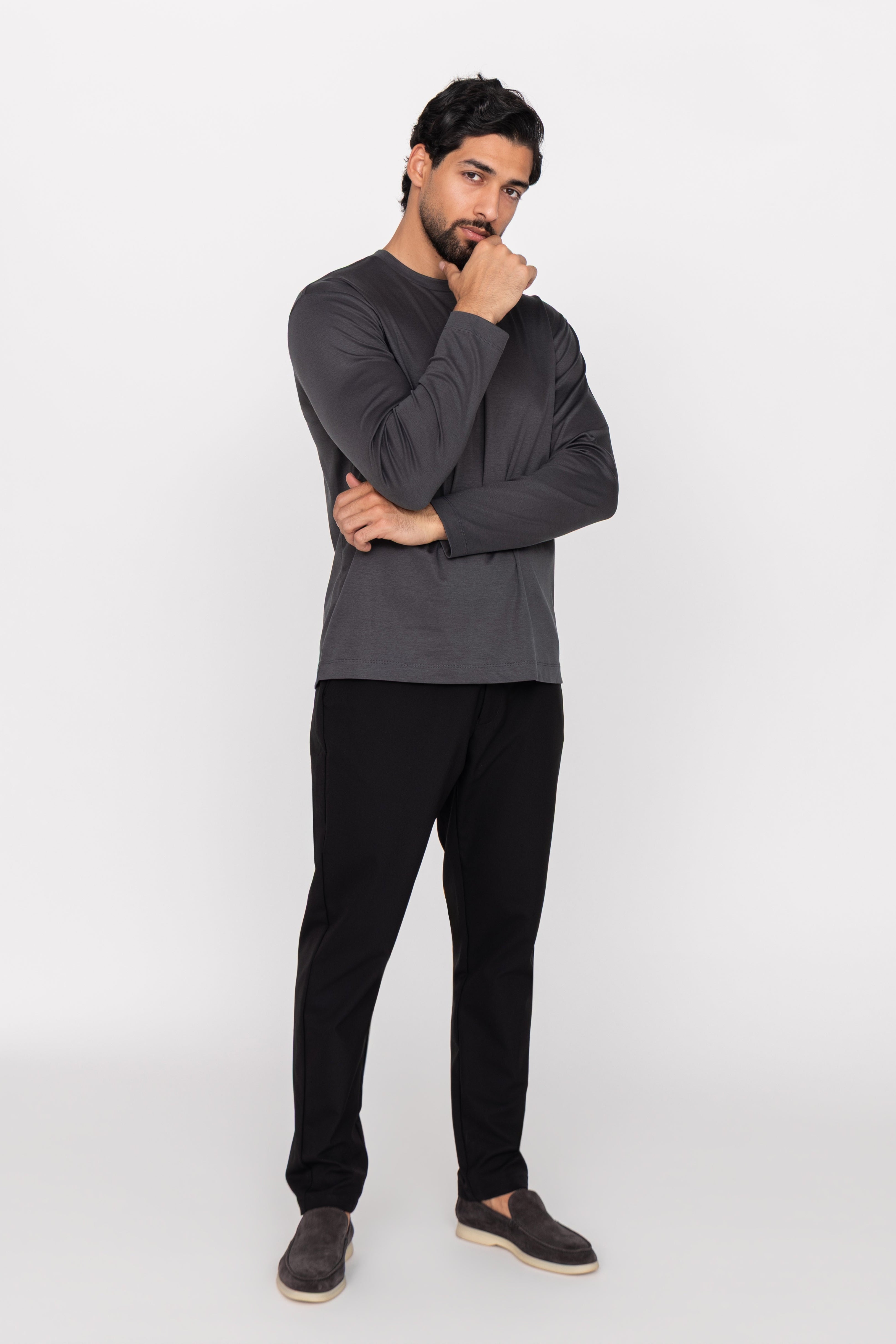 Man wearing a dark gray long-sleeve shirt and black pants on a white background
