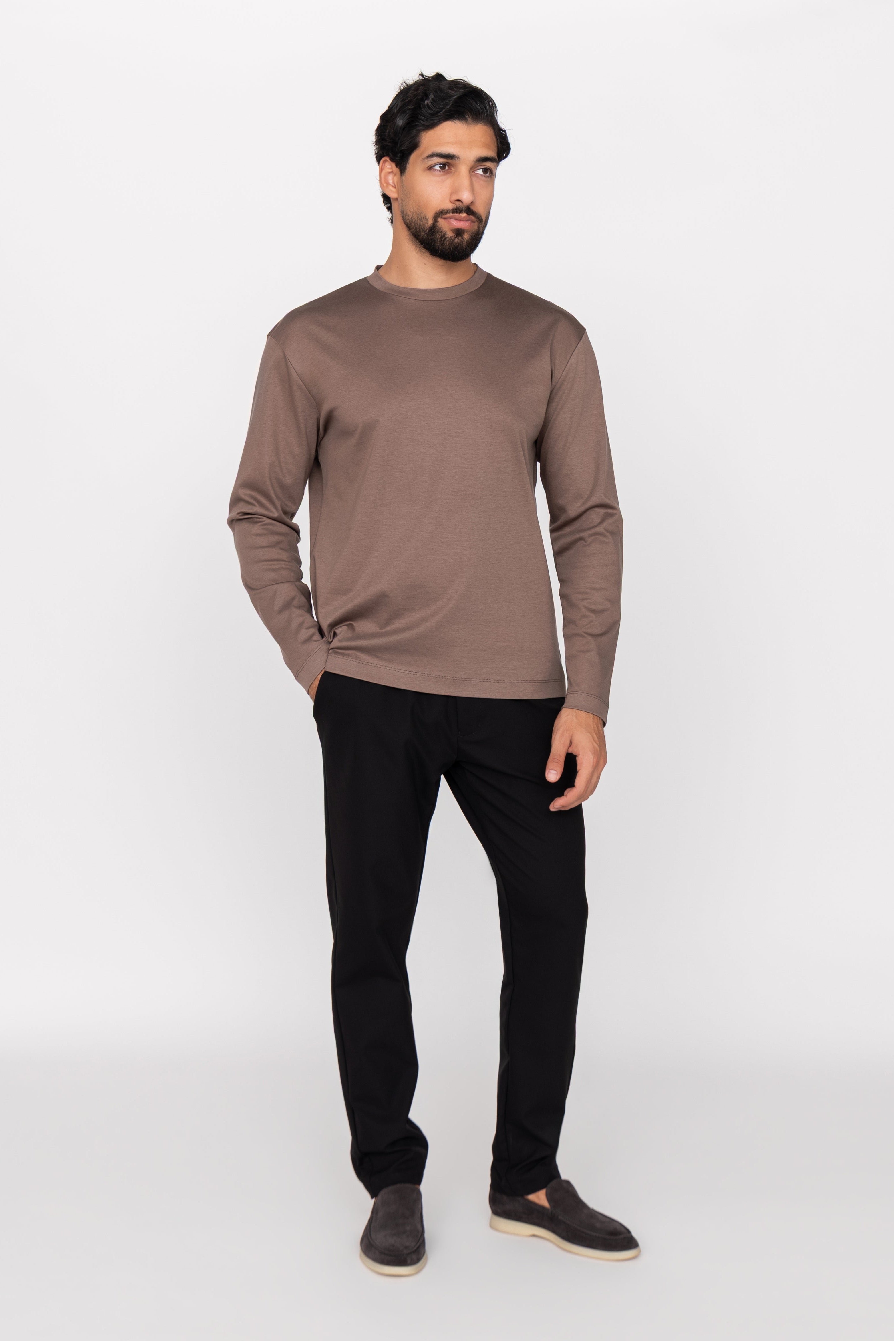 Man wearing a brown long-sleeve shirt and black pants on a white background