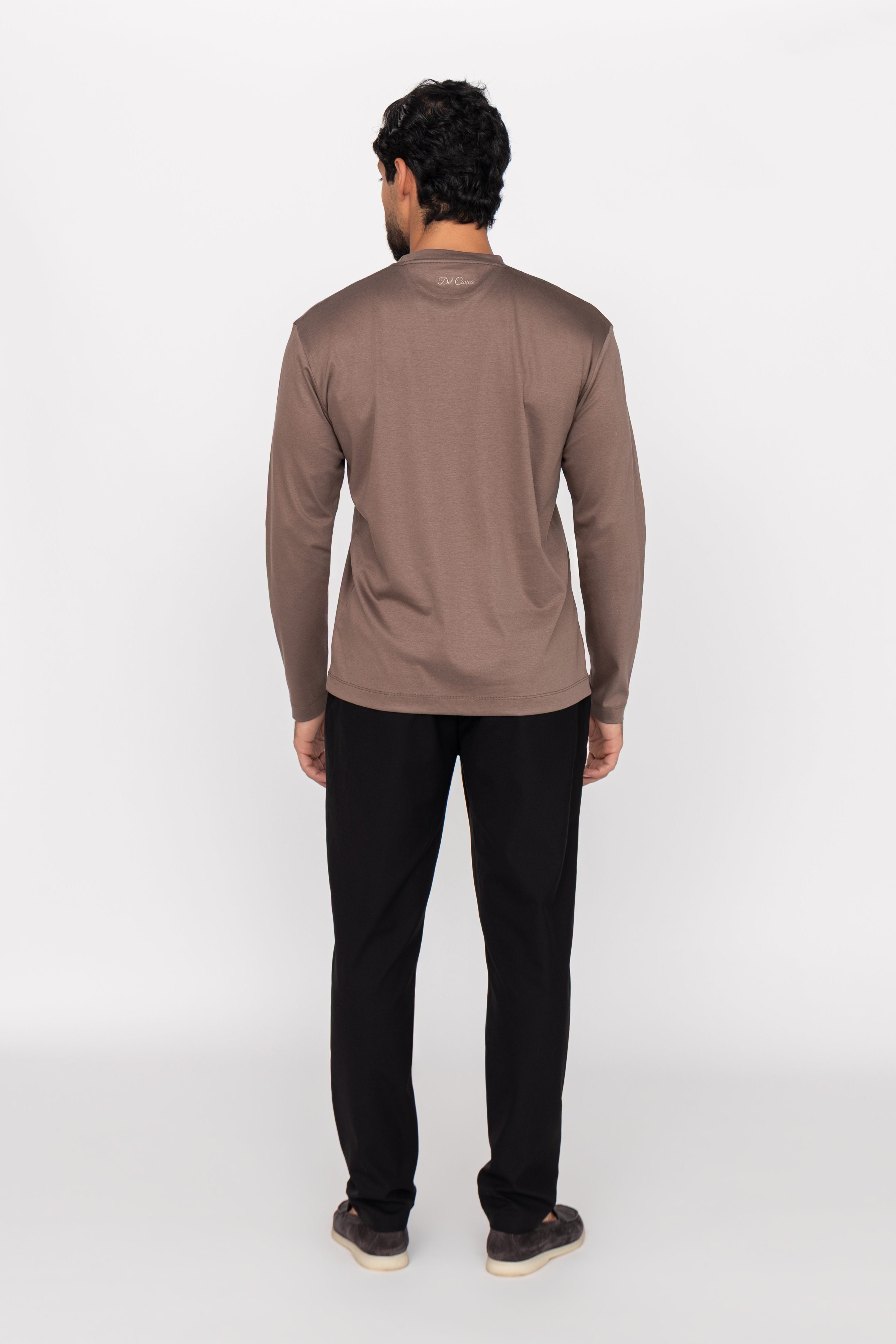 Man wearing a brown long-sleeve shirt and black pants on a white background