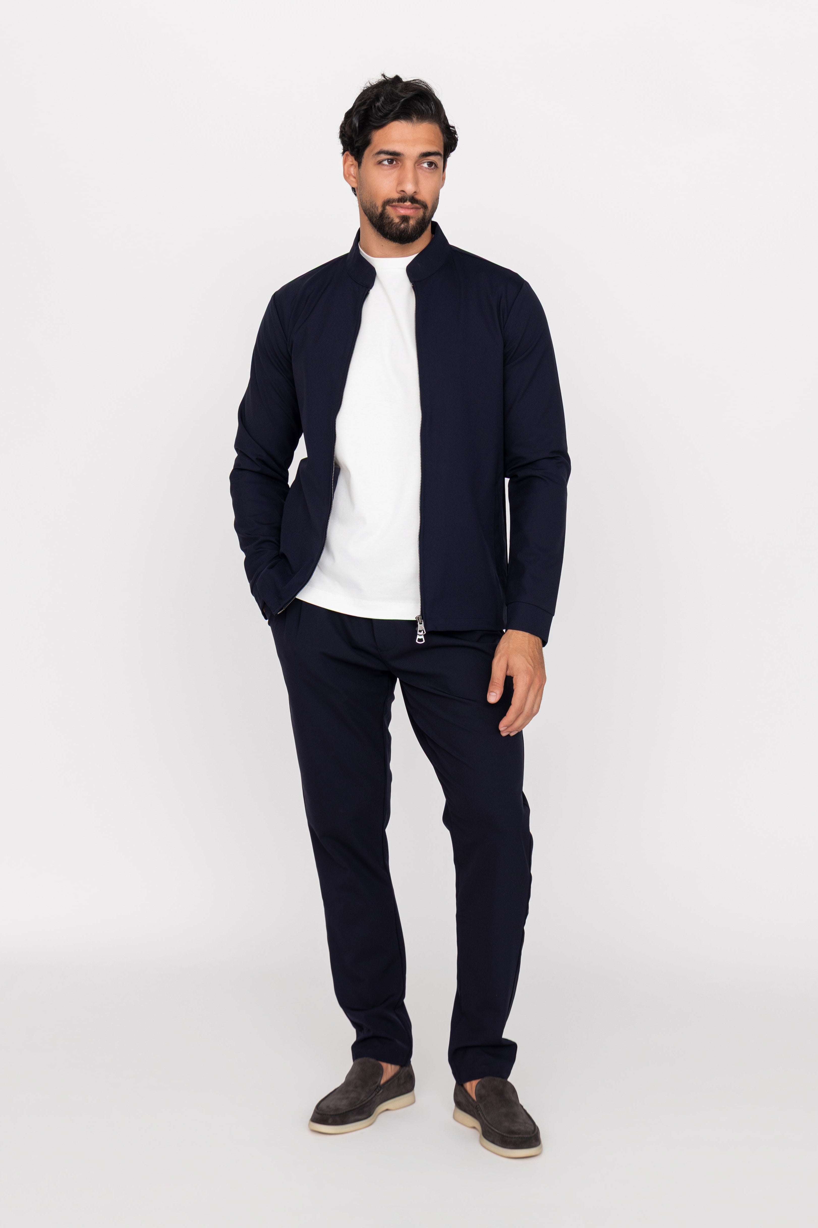Man wearing a navy cardigan, white shirt, and dark pants on a white background